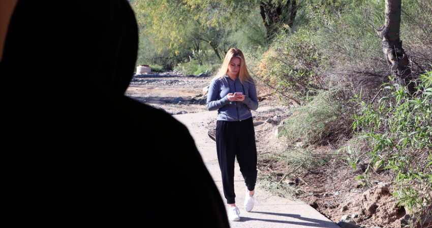 person in black hoodie watching woman walk looking down on her phone