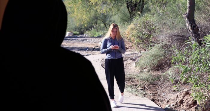 person in black hoodie watching woman walk looking down on her phone